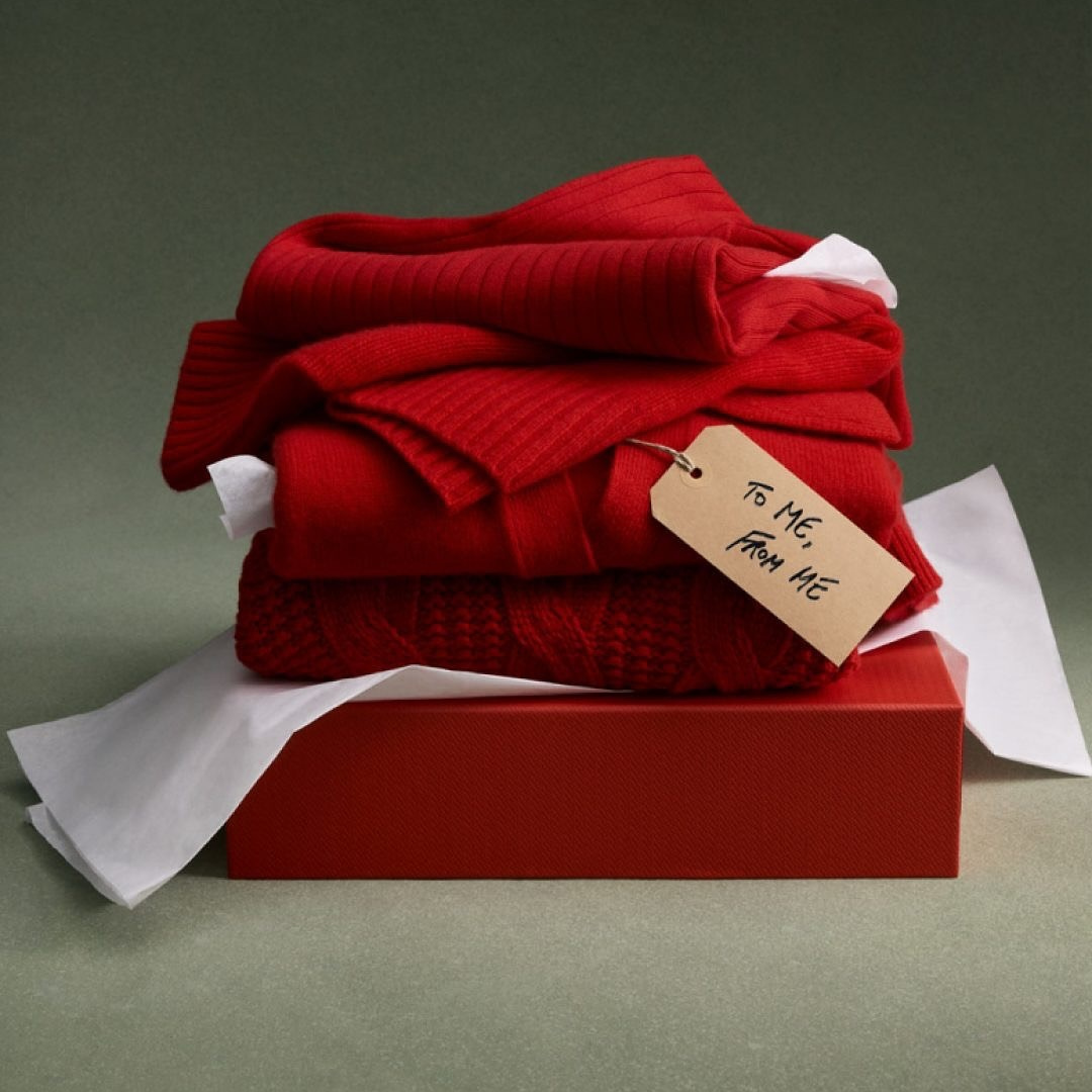 Three folded red sweaters sitting on a red gift box with a tag saying "To Me From Me"